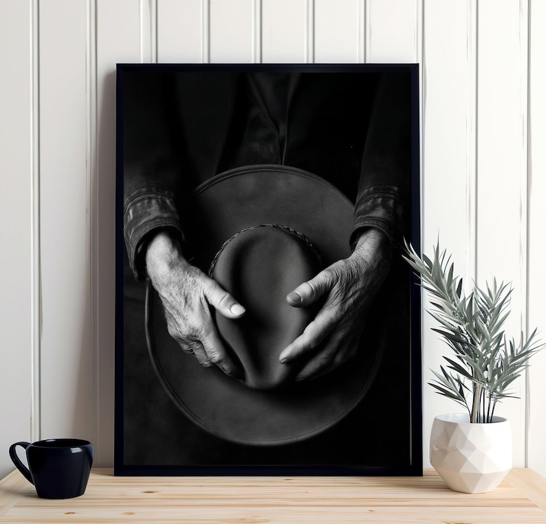 Pu&ograve; includere: Fotografia in bianco e nero di mani che tengono un cappello a tesa larga. Il cappello &egrave; fatto di un materiale scuro e ha una superficie leggermente strutturata. Le mani della persona sono rugose e mostrano segni di et&agrave;.