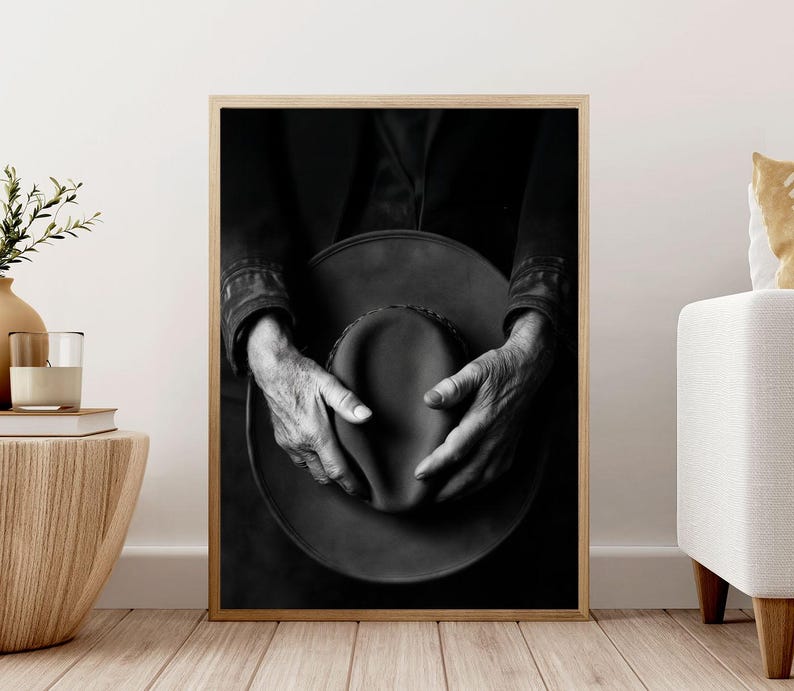 Pu&ograve; includere: Fotografia in bianco e nero di mani che tengono un cappello a tesa larga. Il cappello &egrave; fatto di un materiale scuro e ha una superficie leggermente strutturata. Le mani della persona sono unite intorno al cappello e le sue dita sono visibili.