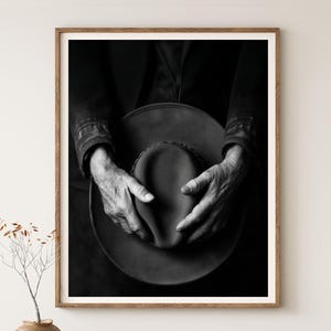 Pu&ograve; includere: Una fotografia in bianco e nero di mani che tengono un cappello a tesa larga. Il cappello &egrave; fatto di un materiale strutturato e le mani della persona sono rugose e mostrano segni di et&agrave;.