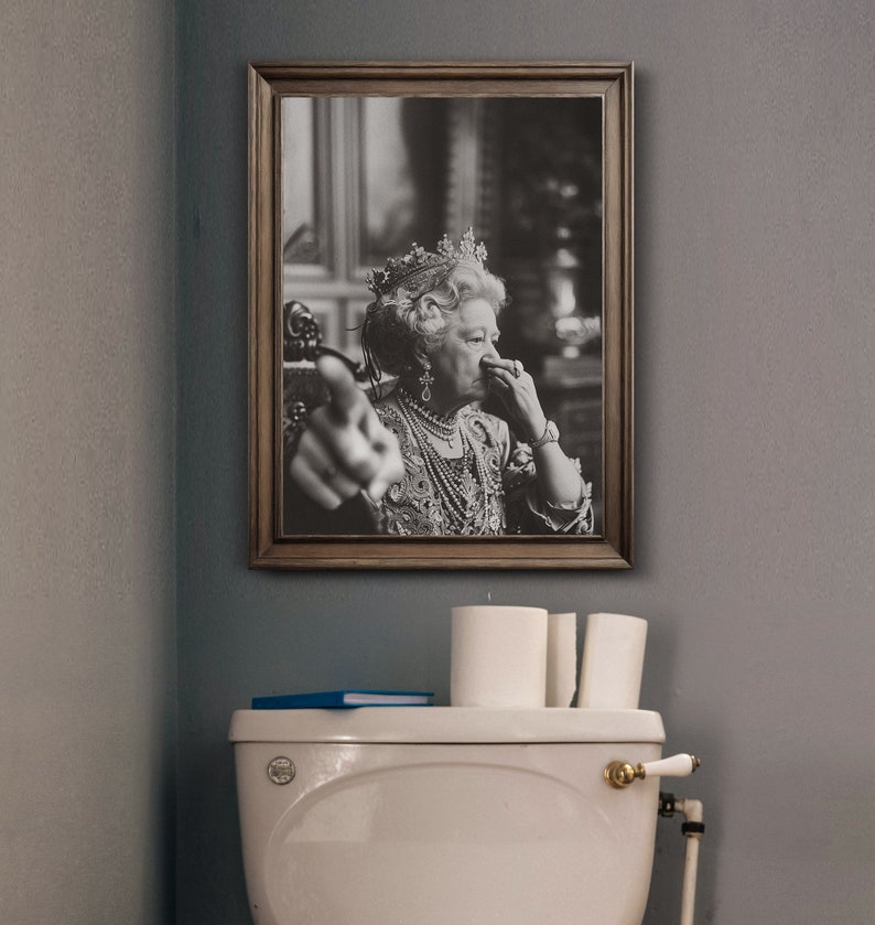 May include: A black and white framed photo of a woman wearing a crown and a pearl necklace. She is holding her nose with her right hand and pointing with her left hand.
