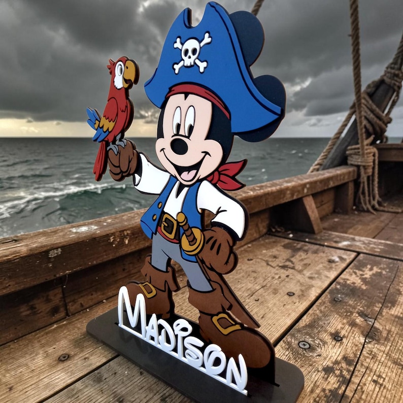 May include: A wooden pirate-themed Mickey Mouse figure with a blue hat, red bandana, and a parrot. The figure is holding a sword and stands on a base with the name "Madison" in white letters. The background shows a cloudy sky and water.