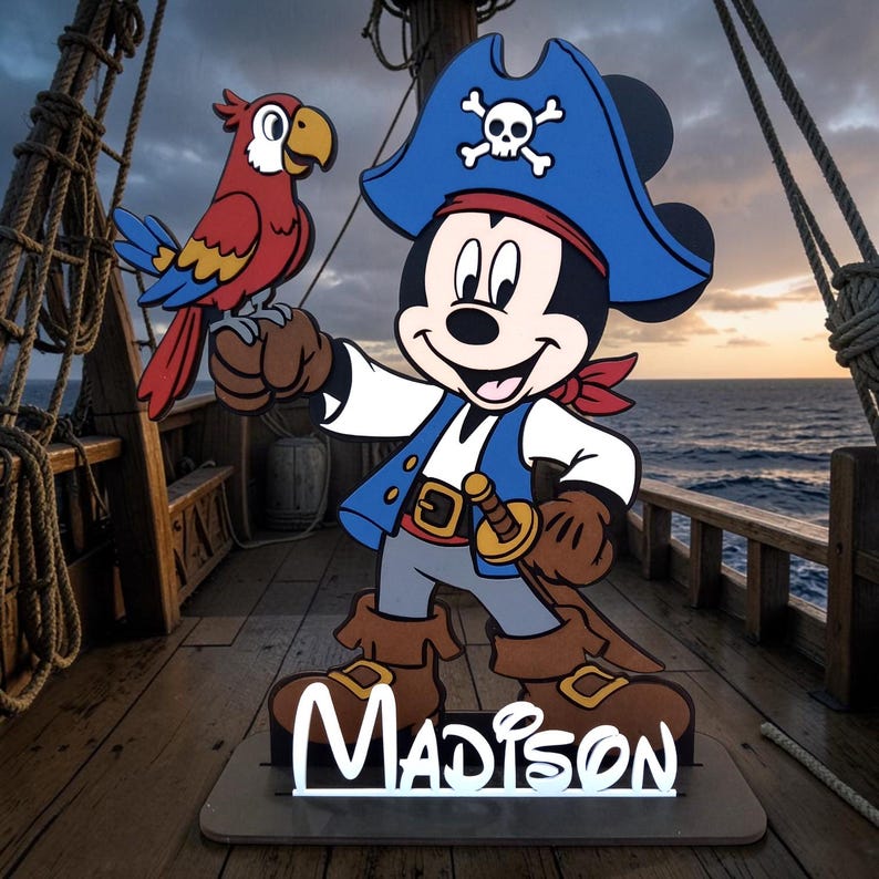 May include: A wooden pirate-themed cutout featuring Mickey Mouse in a blue pirate hat with a skull and crossbones, a red bandana, and a toy sword. A red, blue, and yellow parrot sits on his hand. The name "Madison" is displayed at the base.