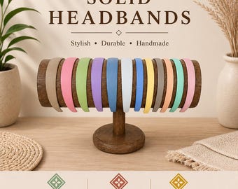 May include: A collection of twelve solid-colored headbands displayed on a horizontal wooden stand. The headbands feature a smooth finish and come in a variety of colors including tan, pink, green, purple, blue, white, yellow, and teal.