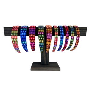 May include: A set of ten colorful headbands with a beaded pattern. The headbands are displayed on a wooden stand.
