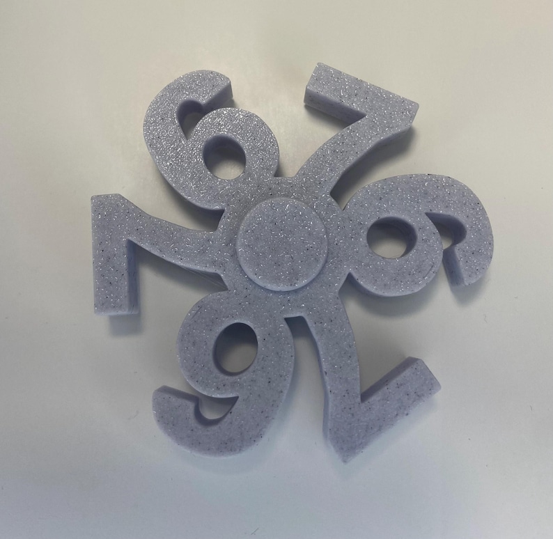 May include: A light purple, six-pointed star-shaped object with the numbers 6, 7, and 9 repeated. The numbers are connected at a central circle. The object has a textured, speckled appearance and is set against a white background.