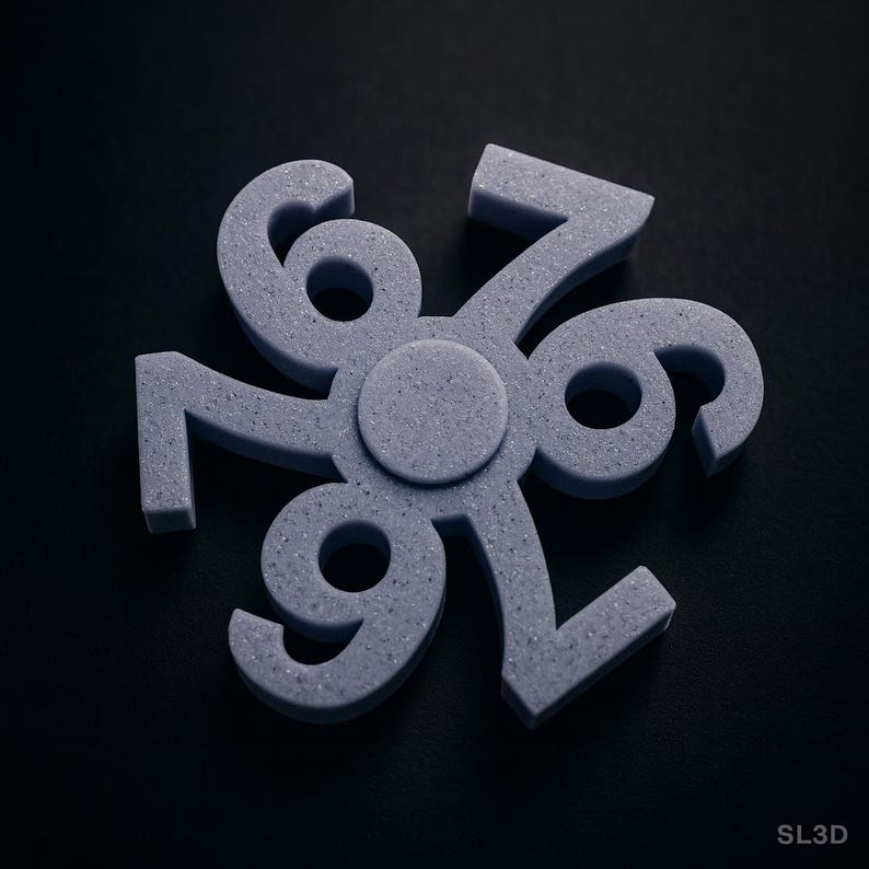 May include: A gray, 3D-printed fidget spinner with the numbers 6, 7, and 9 arranged in a circular pattern. The numbers are connected at a central hub. The background is black.
