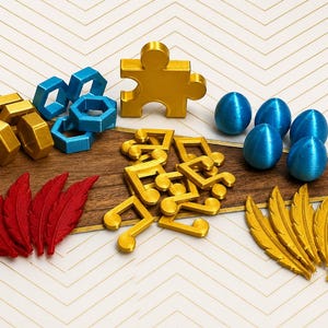May include: An assortment of colorful, 3D-printed objects. Includes gold puzzle piece, blue and gold geometric shapes, red and gold feathers, blue eggs, and gold musical notes. The items are arranged on a wooden surface with a white and gold chevron pattern background.