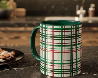 May include: A ceramic mug with a green handle and interior. The exterior features a white background with a plaid pattern in green and red. The mug is sitting on a dark countertop.