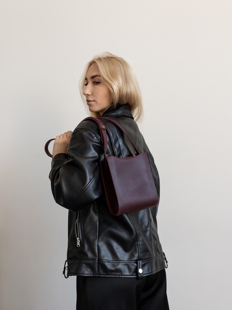 Pode incluir: Uma bolsa de couro bord&ocirc; com um design estruturado. A bolsa tem uma al&ccedil;a curta e uma al&ccedil;a de ombro. A pessoa na imagem est&aacute; usando uma jaqueta de couro preta.