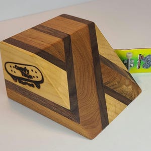 Peut inclure: Rampe de fingerboard en bois avec un design géométrique, composée de panneaux de bois clairs et foncés. La rampe porte le logo "Comfy Town" et est associée à un fingerboard jaune. La rampe est conçue pour les figures de fingerboard.