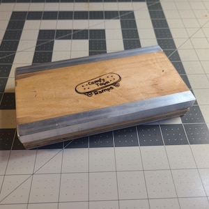 Puede incluir: Una rampa de madera con un borde de metal plateado. La rampa tiene un logotipo que dice "Comfy Town Ramps" con un gráfico de patineta.