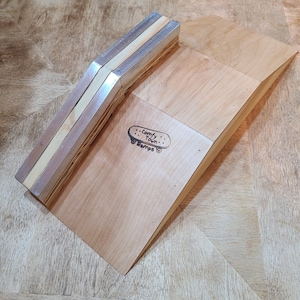 May include: A wooden ramp with a metal lip, designed for skateboarding. The ramp is made of plywood and has a natural wood finish. The metal lip is made of aluminum and is attached to the ramp with screws. The ramp is labeled "Comfy Town Ramps".