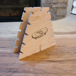 Pode incluir: Uma rampa de madeira para fingerboards, feita de madeira clara com um logotipo gravado a laser que diz "Comfy Town Ramps".