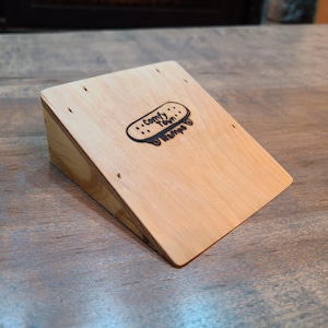 Könnte beinhalten: Eine Holzrampe zum Fingerboarden mit einem schwarz-weißen Logo, auf dem "Comfy Town Ramps" steht.