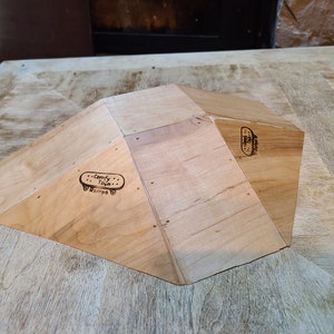 May include: A wooden fingerboard ramp with a triangular shape and a "Comfy Town Ramps" logo. The ramp is made of light wood and has a natural finish.