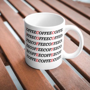 Könnte beinhalten: Weiße Keramik-Kaffeetasse mit dem Wort "COFFEE" wiederholt in schwarzer Schrift mit roten "C"s.