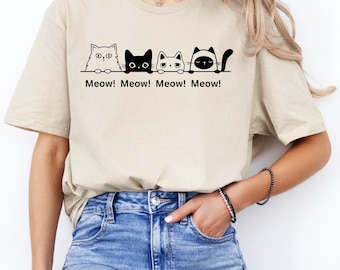 May include: A beige t-shirt with a graphic of four cats peeking over a line with the text "Meow! Meow! Meow! Meow!"