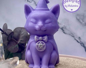 Peut inclure: Une bougie violette en forme de chat portant un chapeau pointu et une cape avec un nœud pailleté et un pendentif circulaire orné d'une étoile. La bougie a une mèche sur le dessus et un logo circulaire avec le texte designed by Melumino.