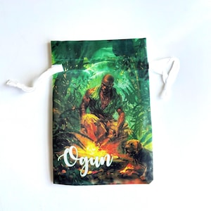 May include: A green drawstring bag with a jungle scene featuring a man with a dog. The bag has the word "Ogun" written in white cursive.