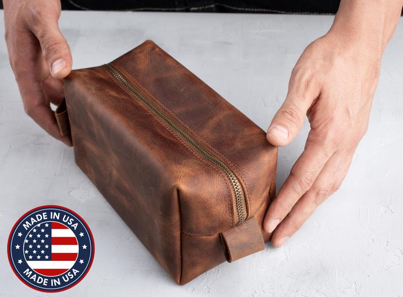 Peut inclure: Une trousse de toilette en cuir marron avec une fermeture &eacute;clair et une poign&eacute;e en cuir. Le sac est fabriqu&eacute; aux &Eacute;tats-Unis.