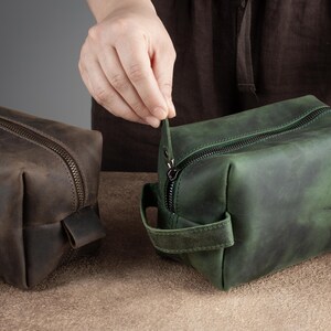 Peut inclure: Deux sacs de voyage en cuir, l'un brun et l'autre vert, avec des fermetures &eacute;clair et des poign&eacute;es. Le sac vert est ouvert et la fermeture &eacute;clair est tir&eacute;e par une main.