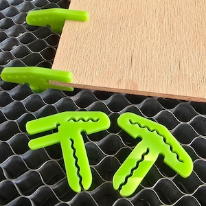 May include: Green plastic corner clamps for woodworking projects. The clamps are designed to hold pieces of wood together at a 90-degree angle.