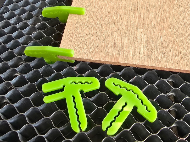 May include: Green plastic corner clamps for woodworking projects. The clamps are designed to hold pieces of wood together at a 90-degree angle.