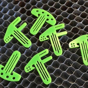 May include: Six bright green plastic T-shaped pieces with holes and grooves. These pieces are designed to be used as a tool or a part of a larger object.
