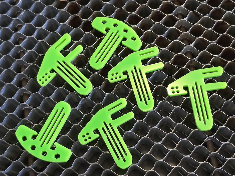 May include: Six bright green plastic T-shaped pieces with holes and grooves. These pieces are designed to be used as a tool or a part of a larger object.