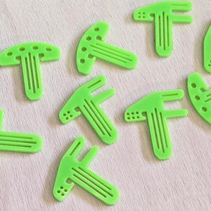 May include: Nine lime green plastic T-shaped pieces with a raised design. The pieces are arranged in a scattered pattern on a light wood surface.