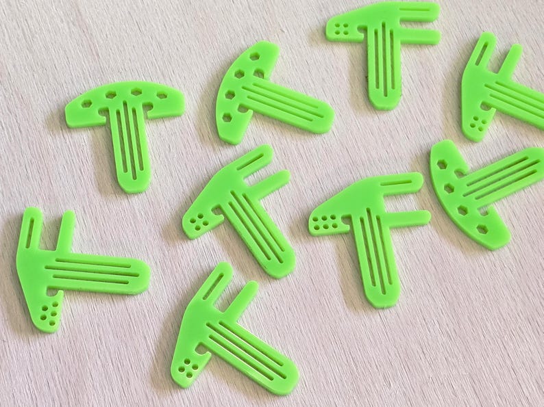 May include: Nine lime green plastic T-shaped pieces with a raised design. The pieces are arranged in a scattered pattern on a light wood surface.
