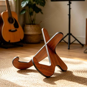 May include: A wooden stand with a brown wood grain finish and black edges, featuring an X-shaped interlocking design. The word Ronnie is engraved on the front panel. The stand consists of two pieces that slot together to form a stable base for devices.