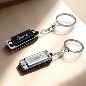 May include: Two harmonica keychains with silver-tone metal and black accents. One keychain has the name "Gracie" engraved, the other has "Joseph". Each keychain has a silver chain and a keyring.