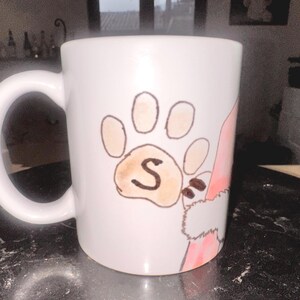 Peut inclure: Une tasse en céramique blanche avec un motif d'empreinte de patte rose et marron. L'empreinte de patte a la lettre "S" au centre.