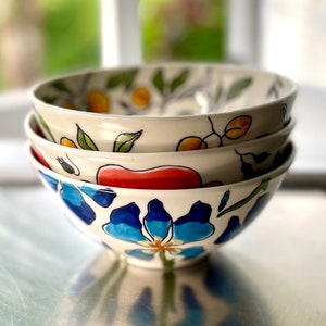 May include: Three ceramic bowls stacked on top of each other. The bowls are decorated with a floral pattern in shades of blue, red, yellow, and green.