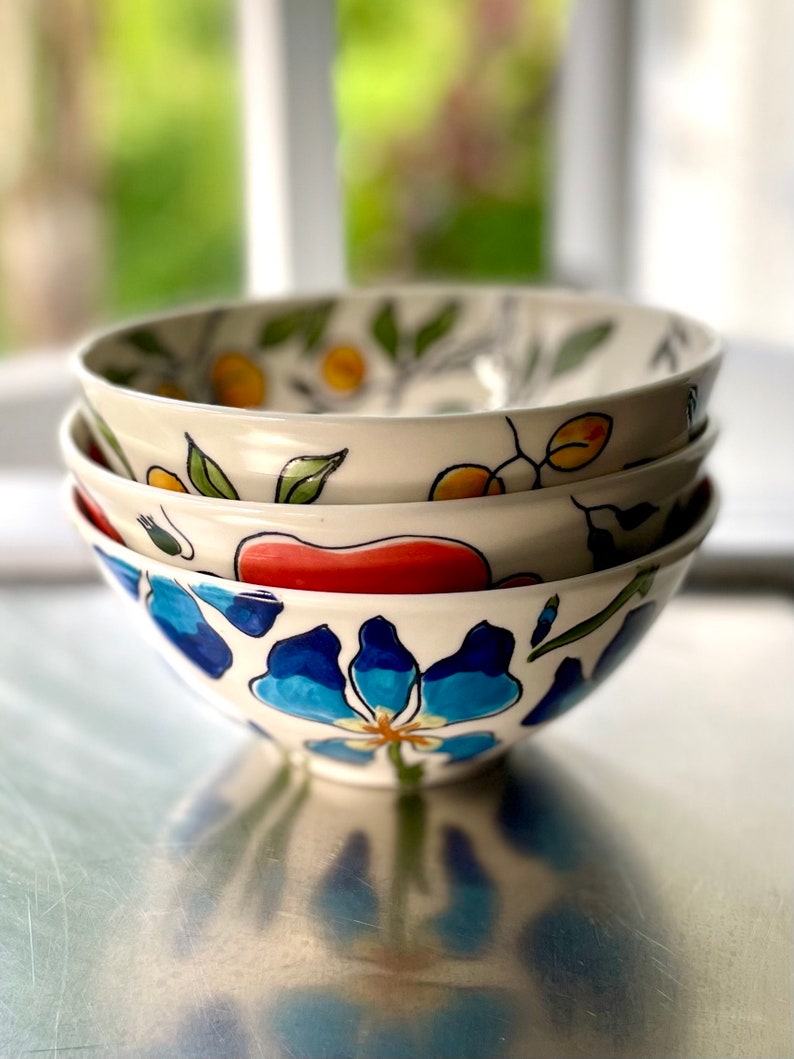 May include: Three ceramic bowls stacked on top of each other. The bowls are decorated with a floral pattern in shades of blue, red, yellow, and green.