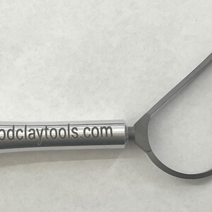 May include: A silver sculpting tool with a triangular loop at the end and a handle with the text "goodclaytools.com" engraved on it.