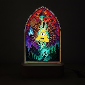 Puede incluir: Una lámpara de acrílico arqueada con una ilustración estilo vitral de un personaje triangular amarillo con un ojo, un sombrero de copa negro y una pajarita. El personaje sostiene llamas azules sobre un fondo de bosque, casa y símbolos.