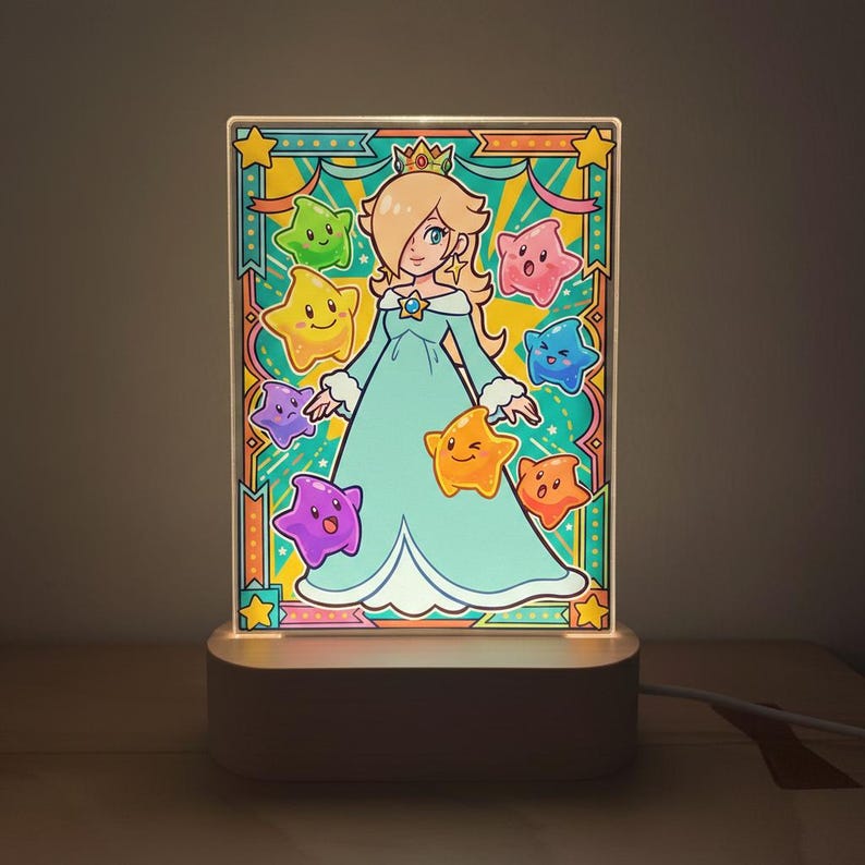 Op de afbeelding: Een verlicht acryl paneel met een cartoonprinses in een blauwe jurk, omringd door kleurrijke sterren. Het paneel staat op een witte basis met een netsnoer, waardoor een decoratief nachtlampje ontstaat.