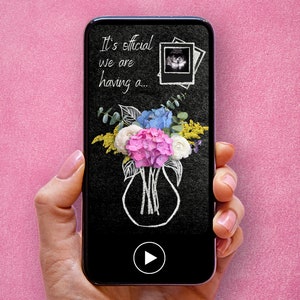 Puede incluir: Una pantalla de teléfono inteligente que muestra un fondo negro con dibujos de tiza blanca de un ramo de flores en un jarrón y el texto "It's official we are having a..." con una pequeña imagen de ultrasonido en la esquina superior derecha. Un botón de reproducción es visible en la parte inferior de la pantalla.