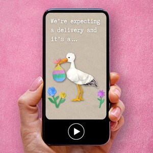 May include: A smartphone screen displaying a digital baby announcement card with a stork carrying a colorful egg. The text on the card reads "We're expecting a delivery and it's a..." with a play button below.