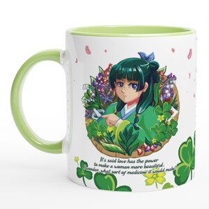 May include: White ceramic mug with a green handle and interior. The mug features an anime-style illustration of a woman in green clothing surrounded by flowers. Text on the mug reads, "It's said love has the power to make a woman more beautiful. I wonder, what sort of medicine it would make?"