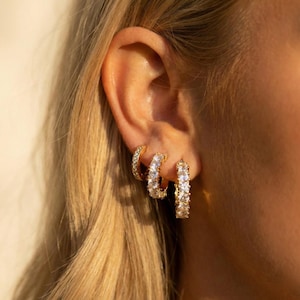 Könnte beinhalten: Nahaufnahme von drei goldenen Creolen. Der kleinste Reifen ist mit kleinen, klaren Steinen besetzt. Der mittlere Reifen ist größer und weist eine Reihe klarer, rechteckiger Steine auf. Der größte Reifen ist ebenfalls goldfarben und weist klare, rechteckige Steine auf.