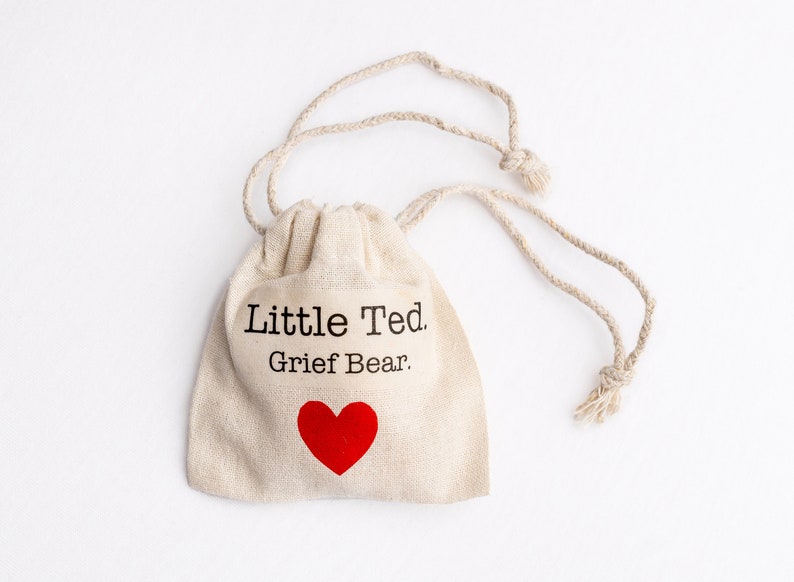 Puede incluir: Una peque&ntilde;a bolsa de tela beige con el texto "Little Ted. Grief Bear." impreso en la parte delantera. Un coraz&oacute;n rojo est&aacute; impreso debajo del texto.
