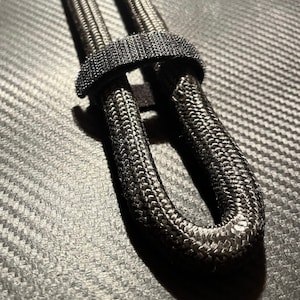 Peut inclure: Cordon tressé noir avec une sangle en velcro noire. La corde est bouclée et fixée avec la sangle.