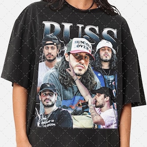 May include: Black t-shirt featuring a graphic of the musician Russ and several images of him. The word "RUSS" is printed in large, stylized letters at the top. The shirt has a vintage, worn look.