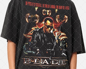 May include: Black t-shirt with a vintage graphic print of the film "Blade". The graphic features a character holding a sword with the text "THE POWER OF AN IMMORTAL, THE SOUL OF A HUMAN, THE HEART OF A HERO." and "BLADE" below the image.