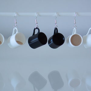 May include: Six pairs of dangle earrings featuring miniature coffee mugs. Two mugs are white with a brown interior, two are black, and two are white with a brown interior.