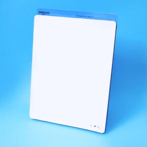 Op de afbeelding: Een wit whiteboard met een blauwe koptekst die "ENDLESS" en "Behoort aan het bureau van..." zegt. Het bord heeft een kleine bel, een hart en een vinkje-icoon in de rechterbenedenhoek.