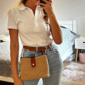 May include: A white collared shirt with a brown leather belt and a brown and beige woven bag with a silver chain strap.